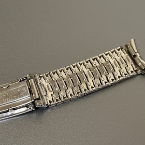 May include: A silver watch band with a clasp that says "Champlain" and "Stainless Steel" on it.