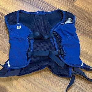 Può includere: Un gilet da idratazione blu reale con un pannello posteriore in rete blu scuro traspirante, due tasche frontali con borracce integrate e cinghie in nylon blu scuro regolabili con fibbie in plastica per una vestibilità sicura sul petto.