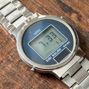 May include: A silver Roxy Digi Solar watch with a blue face and a silver metal band. The watch face displays the time 7:33.