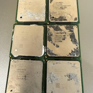 Op de afbeelding: Zes vierkante computerprocessors gerangschikt in twee kolommen van drie. Elke eenheid heeft een groene printplaatbasis en een metalen bovenoppervlak met diverse gegraveerde technische specificaties, waaronder Intel Pentium en Celeron.