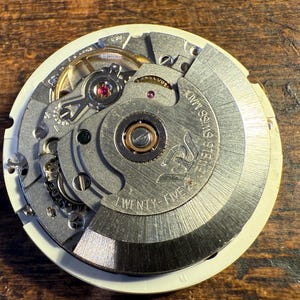 May include: Close-up of a silver watch movement with the text "25 Jewels Swiss Made" and "Twenty-Five" printed on the face.