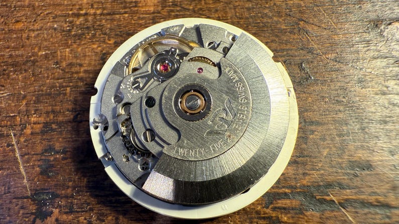 May include: Close-up of a silver watch movement with the text "25 Jewels Swiss Made" and "Twenty-Five" printed on the face.