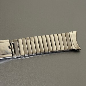 May include: A silver metal watch band with a clasp and a row of links.