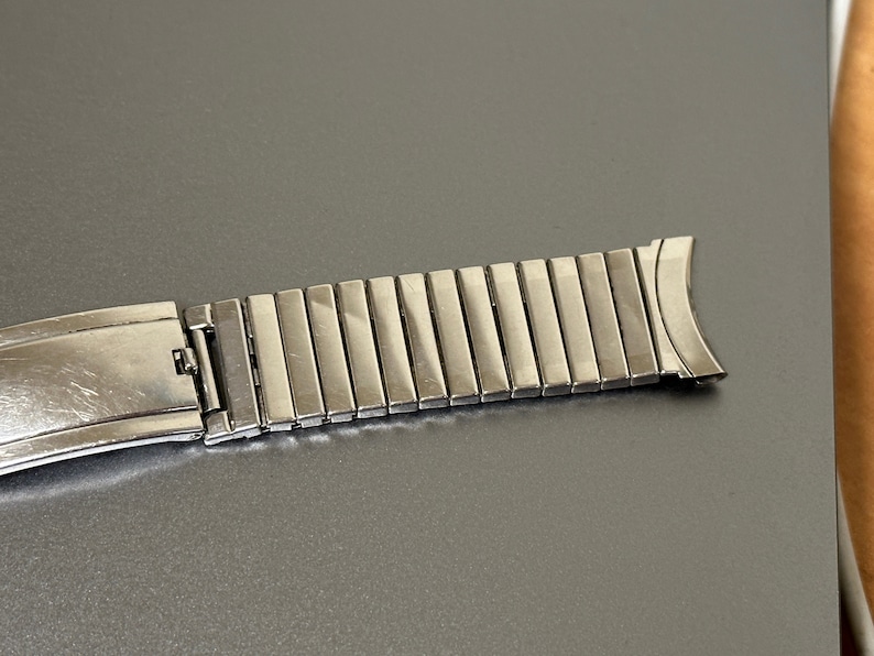 May include: A silver metal watch band with a clasp and a row of links.