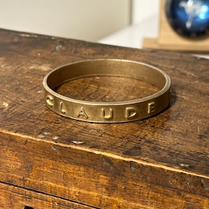 May include: A gold-colored metal ring with the word "CLAUDIE" engraved on it.