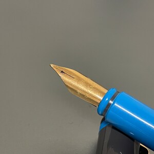 May include: Close-up of a gold-toned fountain pen nib with a blue and silver pen barrel.