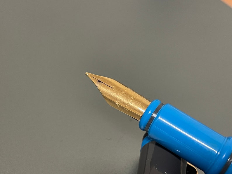May include: Close-up of a gold-toned fountain pen nib with a blue and silver pen barrel.
