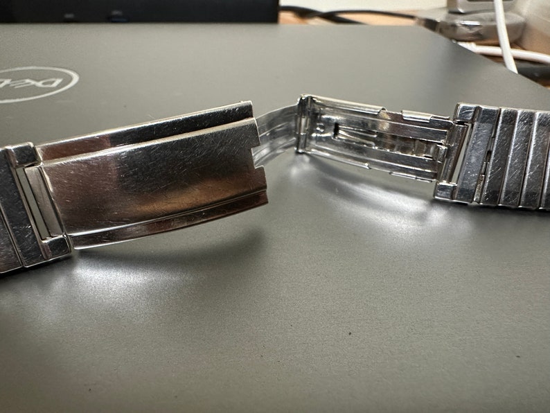 May include: A silver watch band with a clasp that is open. The band is made of metal links.