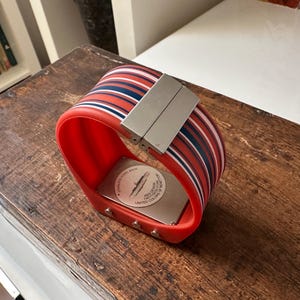 Op de afbeelding: Een rood-zwart gestreept polshorloge met een zilveren metalen band en een witte wijzerplaat. De wijzerplaat van het horloge heeft een onderzee&euml;r-ontwerp en de tekst "Limited Edition" erop.