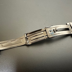 May include: A silver watch band with a clasp that is open. The band is made of metal links.
