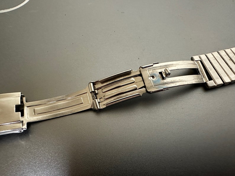 May include: A silver watch band with a clasp that is open. The band is made of metal links.