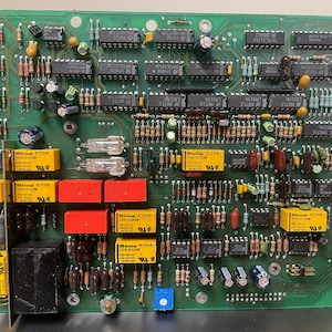 Könnte beinhalten: Eine grüne Leiterplatte mit verschiedenen elektronischen Bauteilen, darunter Widerstände, Kondensatoren, integrierte Schaltkreise und Relais. Die Platine hat ein gelbes Etikett mit dem Text "Audio Precision" und mehrere gelbe und rote Bauteile mit der Bezeichnung "8729A".