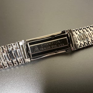 May include: A silver watch band with a clasp that reads "CHAMPION: STAINLESS STEEL U.S.A."