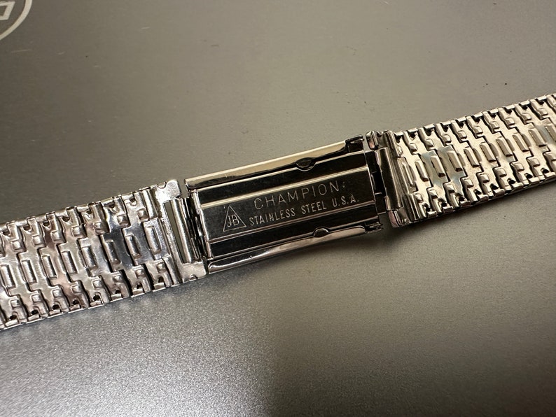 May include: A silver watch band with a clasp that reads "CHAMPION: STAINLESS STEEL U.S.A."