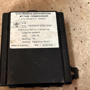 May include: Black electronic control module with a white label featuring German text and technical specifications. The label includes the text "ELEKTRONISCHE WEGFAHRSPERRE" and "Made in Australia".