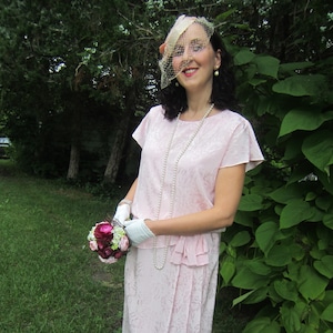 Puede incluir: Una mujer con un vestido rosa con estampado floral sostiene un ramo de flores rosas y burdeos. Lleva un velo blanco y un collar de perlas.