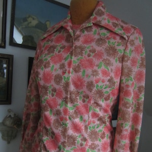 May include: A pink long-sleeved shirt with a large collar and a floral print featuring pink, brown, and green flowers.