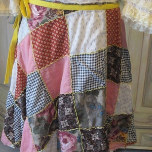 Op de afbeelding: Een patchwork rok met een gele strik. De rok is gemaakt van verschillende stoffen in roze, rood, bruin en wit.