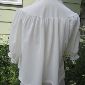 Pode incluir: Uma blusa branca com decote franzido e mangas bufantes. A blusa &eacute; feita de um tecido leve e tem um caimento solto.