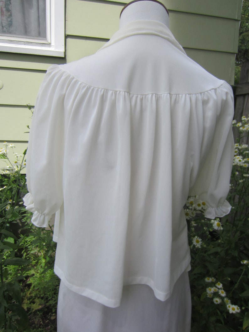 Pode incluir: Uma blusa branca com decote franzido e mangas bufantes. A blusa &eacute; feita de um tecido leve e tem um caimento solto.