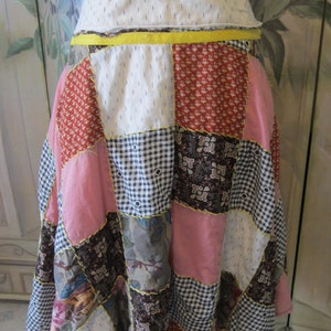 Op de afbeelding: Een patchwork rok met verschillende bloemen- en geometrische patronen in tinten roze, rood, bruin en wit. De rok heeft een gele tailleband en is gemaakt van katoenen stof.