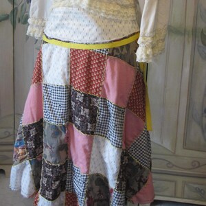 Op de afbeelding: Een patchwork rok met een gele riem. De rok is gemaakt van verschillende stoffen en kleuren, waaronder roze, blauw, bruin en wit.
