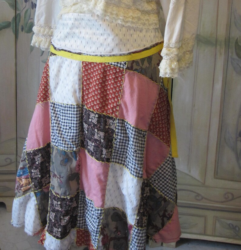 Op de afbeelding: Een patchwork rok met een gele riem. De rok is gemaakt van verschillende stoffen en kleuren, waaronder roze, blauw, bruin en wit.