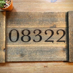 Può includere: Un vassoio da portata in legno con manici in metallo nero. Il vassoio ha una finitura rustica e il numero 08322 è dipinto sul davanti.