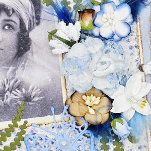 May include: A vintage-style scrapbook page featuring a black and white portrait of a woman. The page is adorned with blue and white paper flowers, blue feathers, and a light blue butterfly cutout with pearl accents. Green decorative edges frame the design.