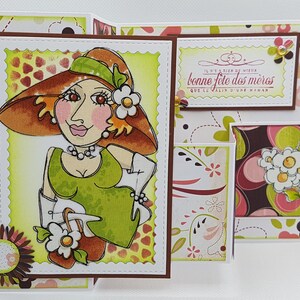 May include: A handmade Mother's Day card featuring a cartoon illustration of a woman in a hat and dress. The card has a scalloped edge and includes the text "Bonne F&ecirc;te des M&egrave;res". Decorative floral patterns and embellishments complete the design.