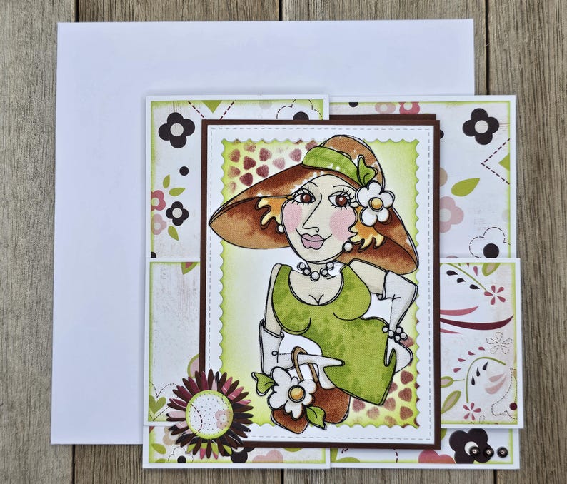 May include: A handmade greeting card featuring a whimsical illustration of a woman in a hat and dress. The card has a layered design with floral and patterned paper accents. The woman is wearing a green dress and a brown hat.