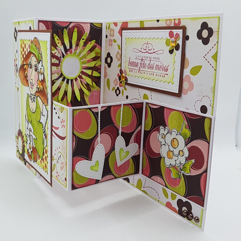 May include: A handmade Mother's Day card with a unique tri-fold design. The card features a cartoon illustration of a woman, floral patterns, and the French text "bonne f&ecirc;te des m&egrave;res". The color palette includes shades of green, brown, pink, and white.