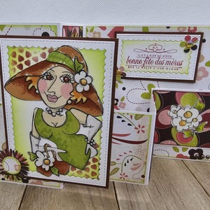 May include: Handmade greeting card featuring a cartoon illustration of a woman in a hat and dress. The card has a floral pattern and the text "bonne f&ecirc;te des m&egrave;res". The card is made of paper and has a brown border.