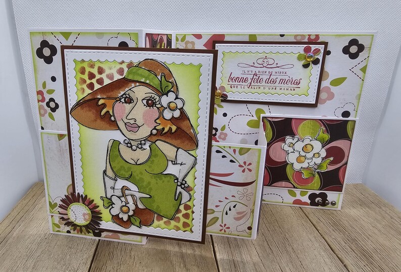 May include: Handmade greeting card featuring a cartoon illustration of a woman in a hat and dress. The card has a floral pattern and the text "bonne f&ecirc;te des m&egrave;res". The card is made of paper and has a brown border.