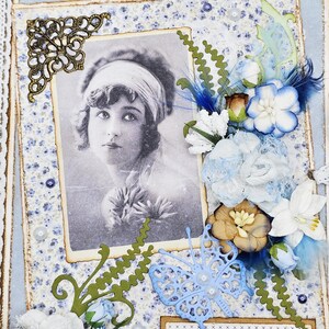 May include: A vintage-style scrapbook page with a black and white portrait of a woman. The page features blue floral patterned paper, lace, and decorative elements like flowers, butterflies, and a quote in French.