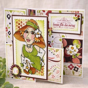 May include: A handmade greeting card featuring a cartoon illustration of a woman in a hat and dress. The card has a floral pattern and includes the text "Bonne F&ecirc;te des M&egrave;res". The card is multi-panel and decorated with embellishments.