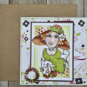 May include: A handmade greeting card featuring a whimsical illustration of a woman in a hat and dress. The card has a brown border and a floral design. The woman is wearing a green dress and holding a white purse with a flower.