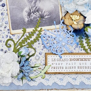 May include: A handmade scrapbook page with a vintage photo, floral embellishments, and a blue butterfly cutout. The page features white lace, blue and white floral patterned paper, and the French text "LE GRAND BONHEUR N'EST FAIT QUE DE PETITS RIENS HEUREUX."