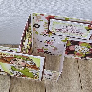 May include: A handmade Mother's Day card with a unique, multi-panel design. The card features a floral pattern in shades of brown, pink, and green. A hand-drawn illustration of a woman in a hat is on the front panel, and the text "Bonne Fete des Meres" is visible.