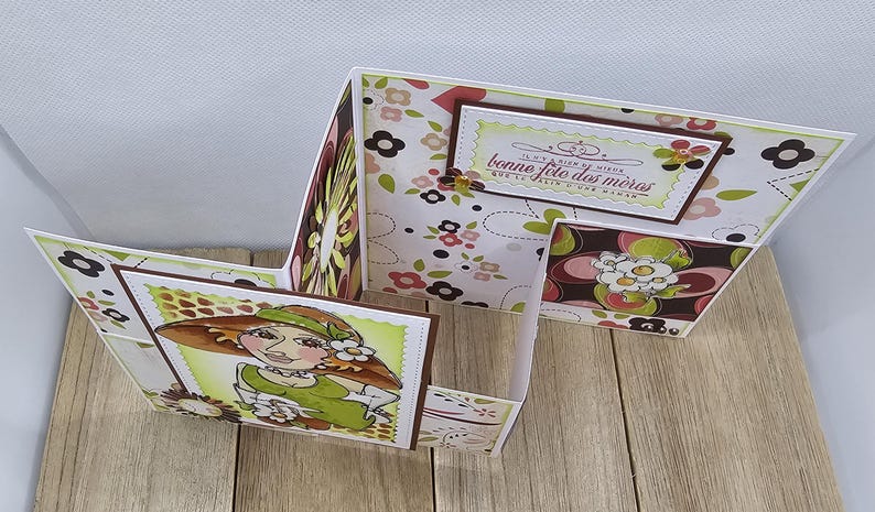 May include: A handmade Mother's Day card with a unique, multi-panel design. The card features a floral pattern in shades of brown, pink, and green. A hand-drawn illustration of a woman in a hat is on the front panel, and the text "Bonne Fete des Meres" is visible.