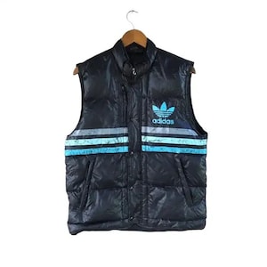 May include: A black puffer vest with a blue and white striped pattern and the Adidas logo on the front.