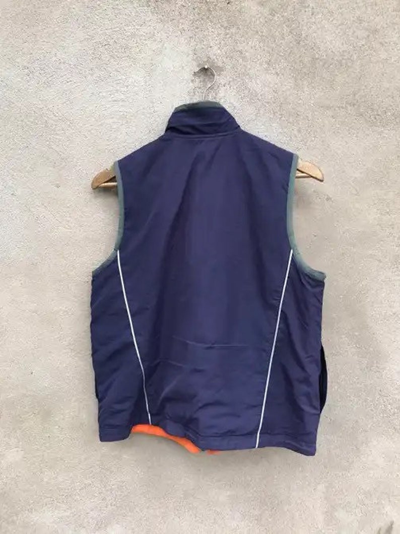 May include: A navy blue vest with white piping and a zipper closure. The vest is hanging on a hanger.