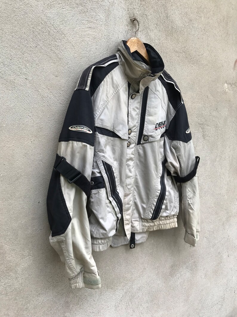 K&ouml;nnte beinhalten: Eine graue und schwarze Skijacke mit Rei&szlig;verschluss und einem schwarz-wei&szlig;en Logo mit der Aufschrift "Cyber Ski".