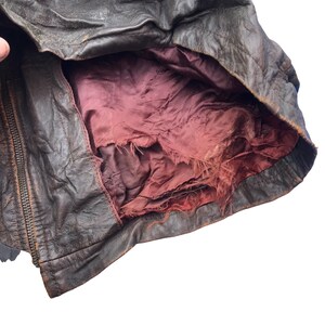 以下が含まれることがあります： 赤い裏地が付いた茶色の革ジャンパー。裏地は破れてほつれています