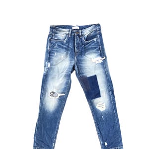 May include: Blue denim jeans with distressed details, including rips and patches. The jeans have a button fly and a classic five-pocket design. The denim has a faded wash.