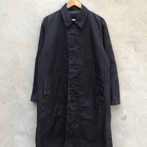 May include: A long black coat with a collar and pockets. The coat is hanging on a hanger.