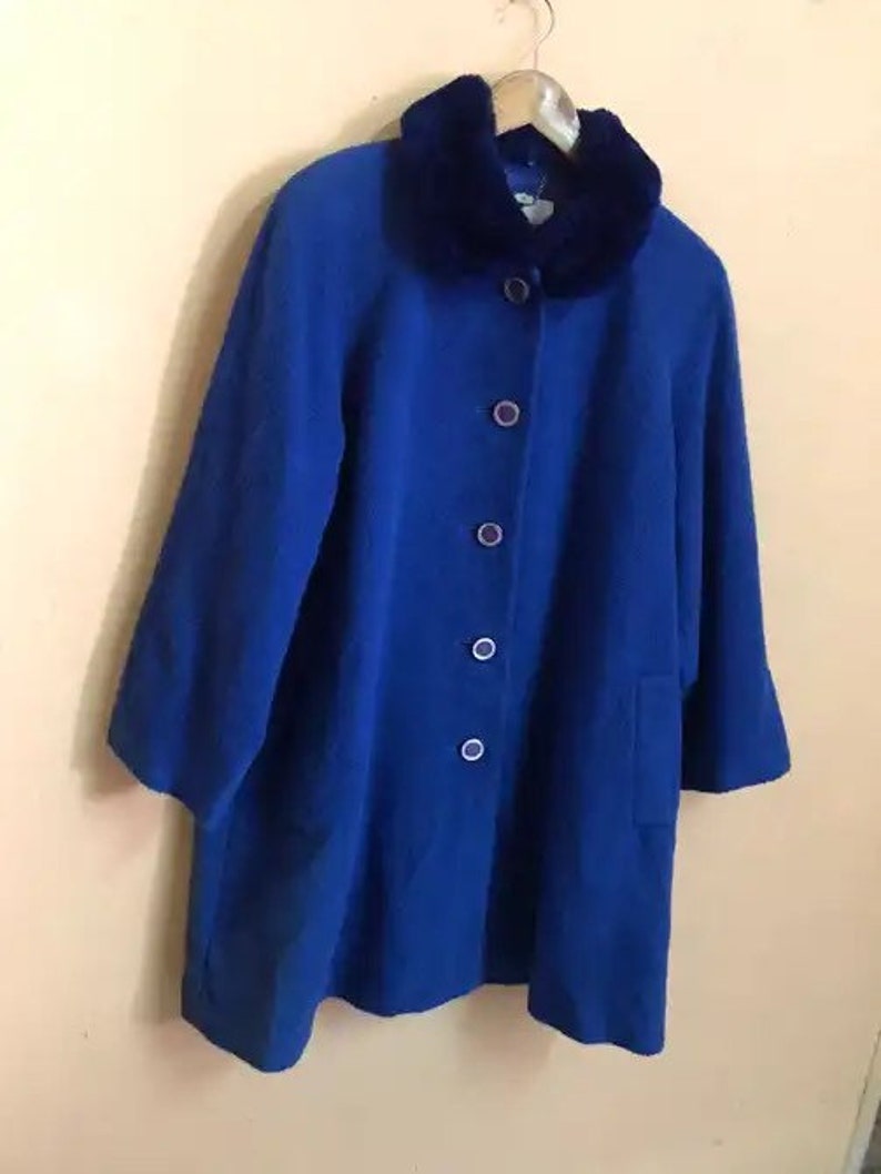 May include: A royal blue wool coat with a large faux fur collar. The coat has a button closure and a single pocket on the left side.