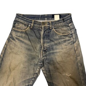 May include: Faded blue denim jeans with a worn appearance. The jeans have a classic five-pocket design, a button closure, and a distressed look with a small tear on the leg. The denim has a vintage wash.