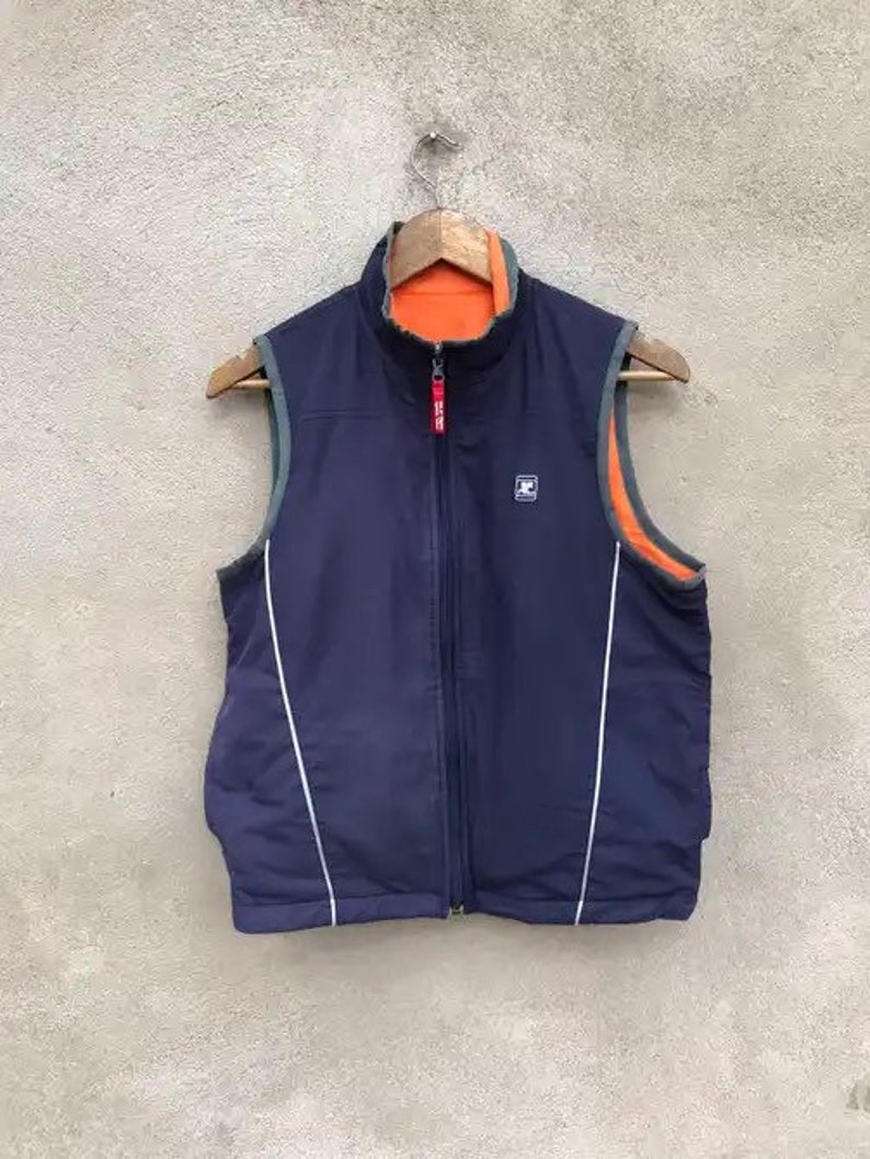 May include: A navy blue reversible vest with white piping and a zipper closure. The vest has a contrasting orange lining.