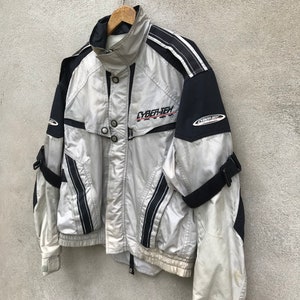 K&ouml;nnte beinhalten: Eine silberne und schwarze Jacke mit dem Aufdruck "CYBER-TECH" auf der Vorderseite. Die Jacke hat schwarze Streifen und einen Rei&szlig;verschluss.